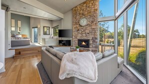 A modern living room with a stone fireplace, a large window, and a cozy seating area. - Bushland (Halls Gap)