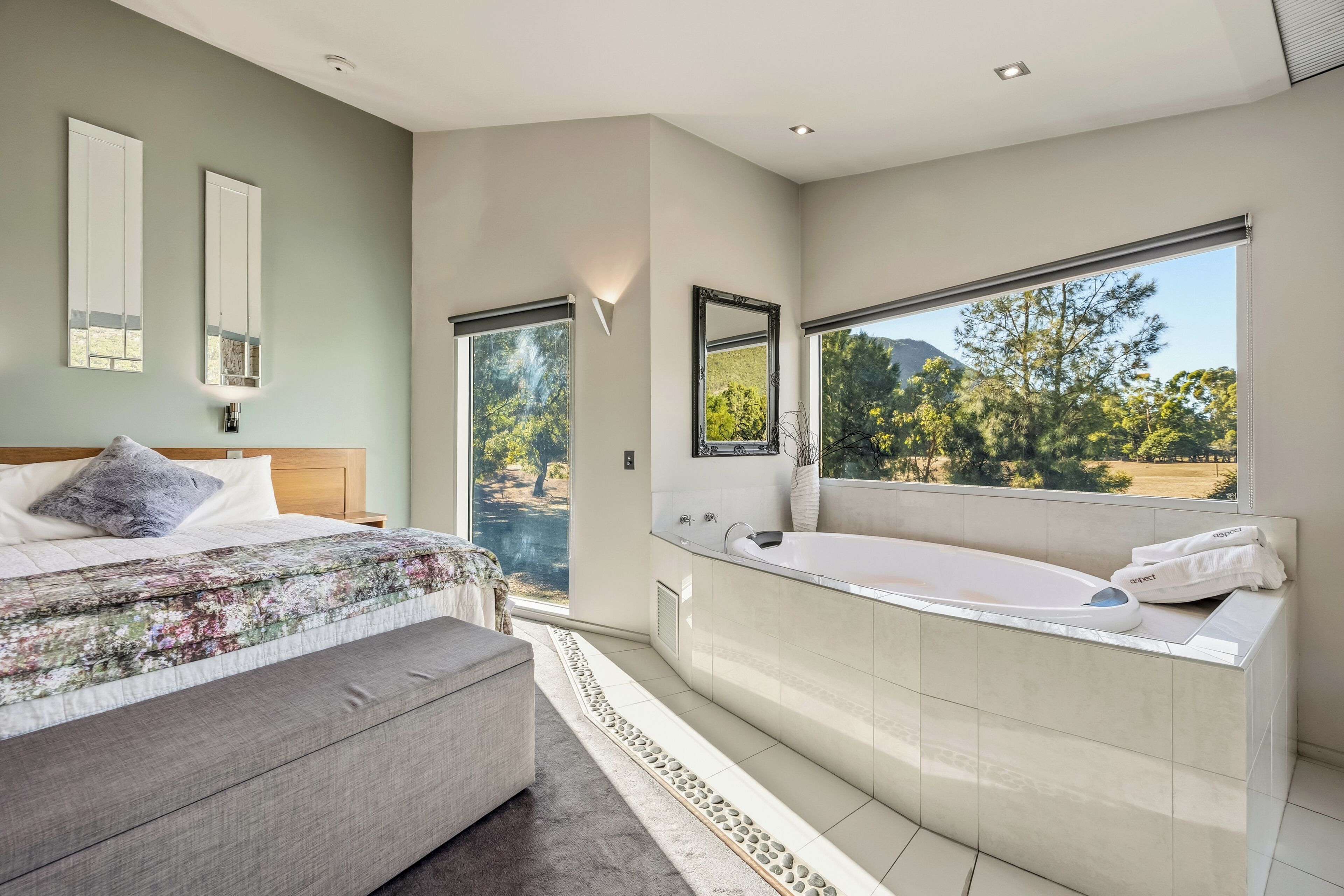 Un dormitorio con una cama grande, una zona de estar, una bañera y vistas al exterior.