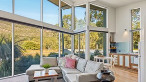 A modern interior with a large glass wall, a sofa, a small table, and a kitchen area. - Bushland (Halls Gap)