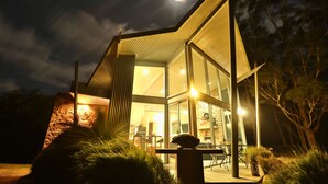 A modern house with a glass facade, a stone exterior, and a well-lit patio area. - Bushland (Halls Gap)