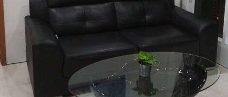 Un sofá de cuero negro, una mesa de centro de vidrio con una planta y un cuadro abstracto colorido en la pared.