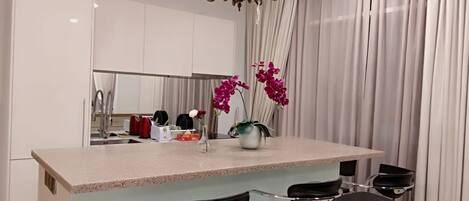 Una cocina moderna con una isla central, taburetes de bar y una lámpara de araña.