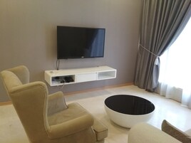 A living room with a flat-screen TV mounted on the wall, a sofa, a coffee table, and a small white shelf below the TV.