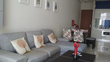 A living room with a grey sofa, a black coffee table, and a kitchen area in the background.