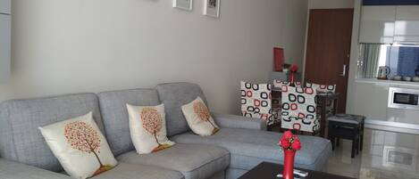 A living room with a grey sofa, a black coffee table, and a kitchen area in the background.