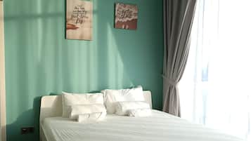 Un dormitorio con pared color turquesa, cama con ropa blanca, dos obras de arte en la pared y una ventana con cortinas.