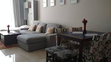 A modern living room with a grey sofa, a dining table with patterned chairs, and a vase with red flowers.