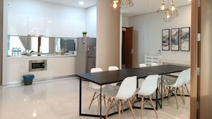 A modern kitchen with white cabinets, a stainless steel refrigerator, and a dining area with a black table and white chairs.