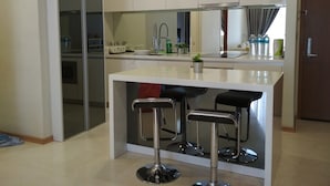 A modern kitchen with a central island, bar stools, and a glass partition.