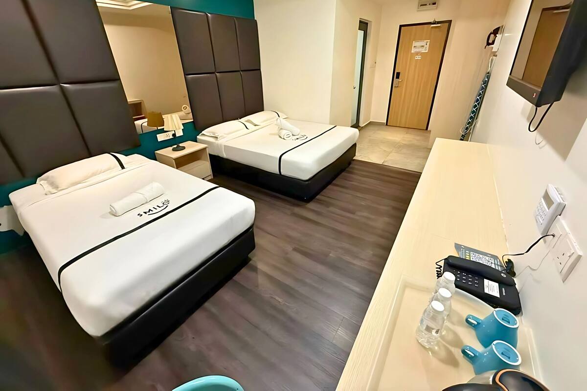 A hotel room with two beds, a bedside table, a mirror, a desk with a phone, and a bathroom door.