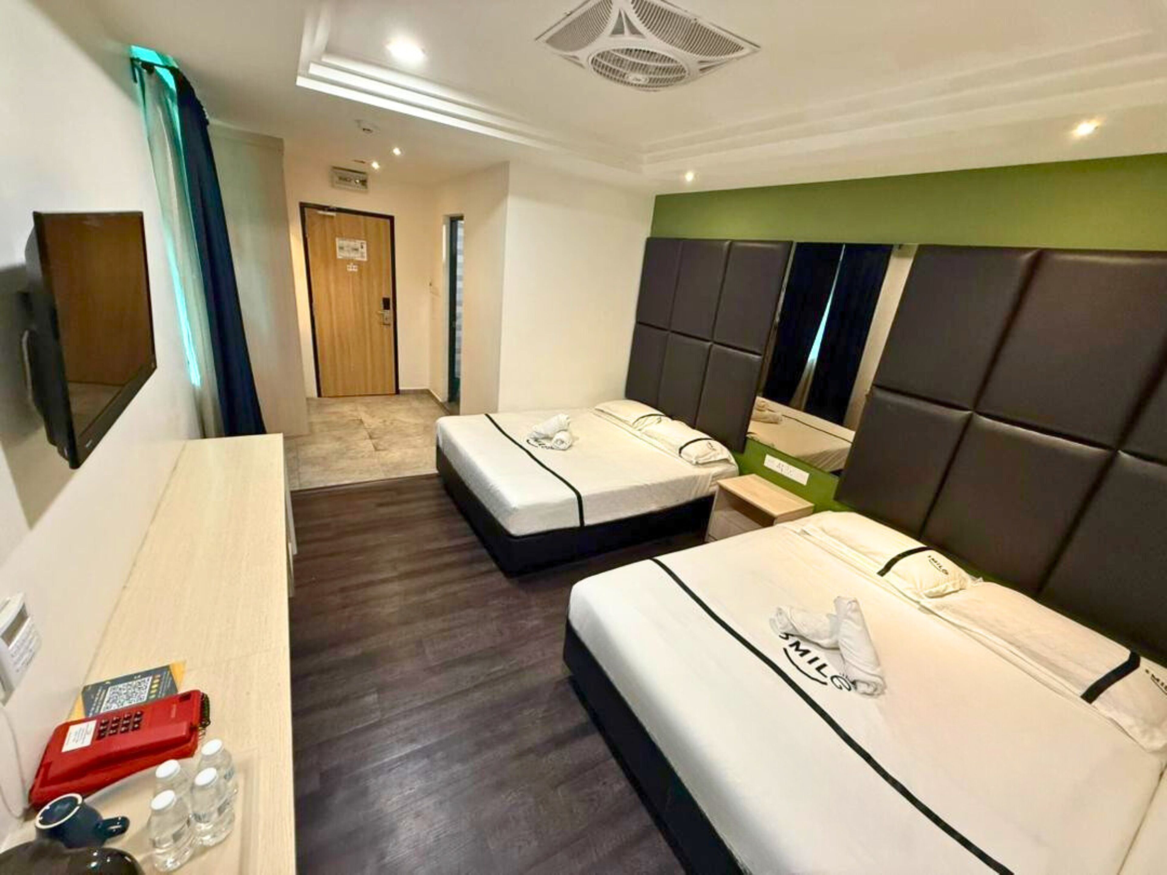 Une chambre d’hôtel avec deux lits, un bureau en bois, un miroir et une porte donnant sur une autre pièce.