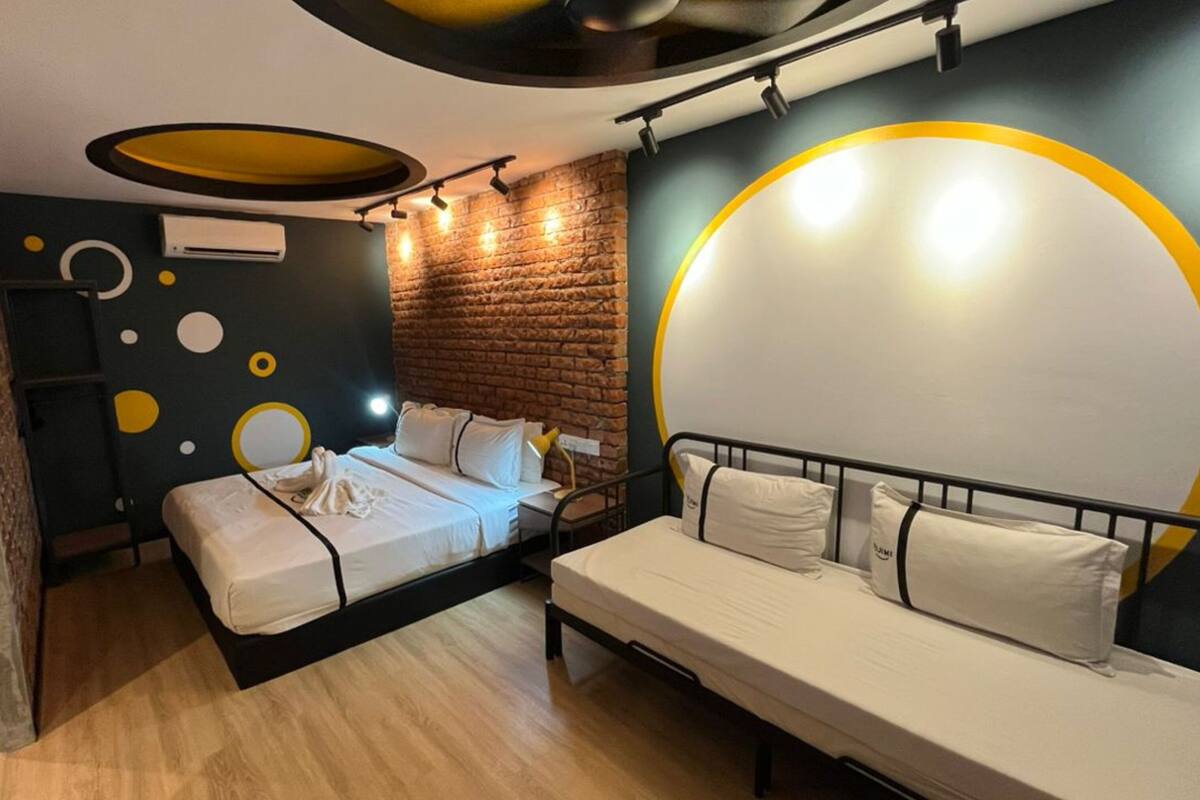 A modern room with a brick accent wall, a bed with white bedding, a bench with pillows, and a large circular light fixture.