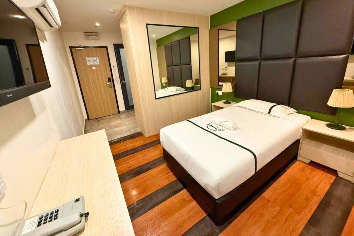 A hotel room with a bed, bedside table, lamp, and a desk with a telephone.