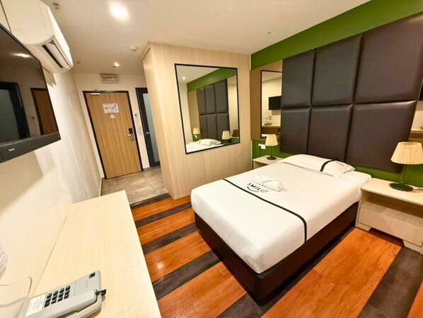 A hotel room with a bed, bedside table, lamp, and a desk with a telephone.