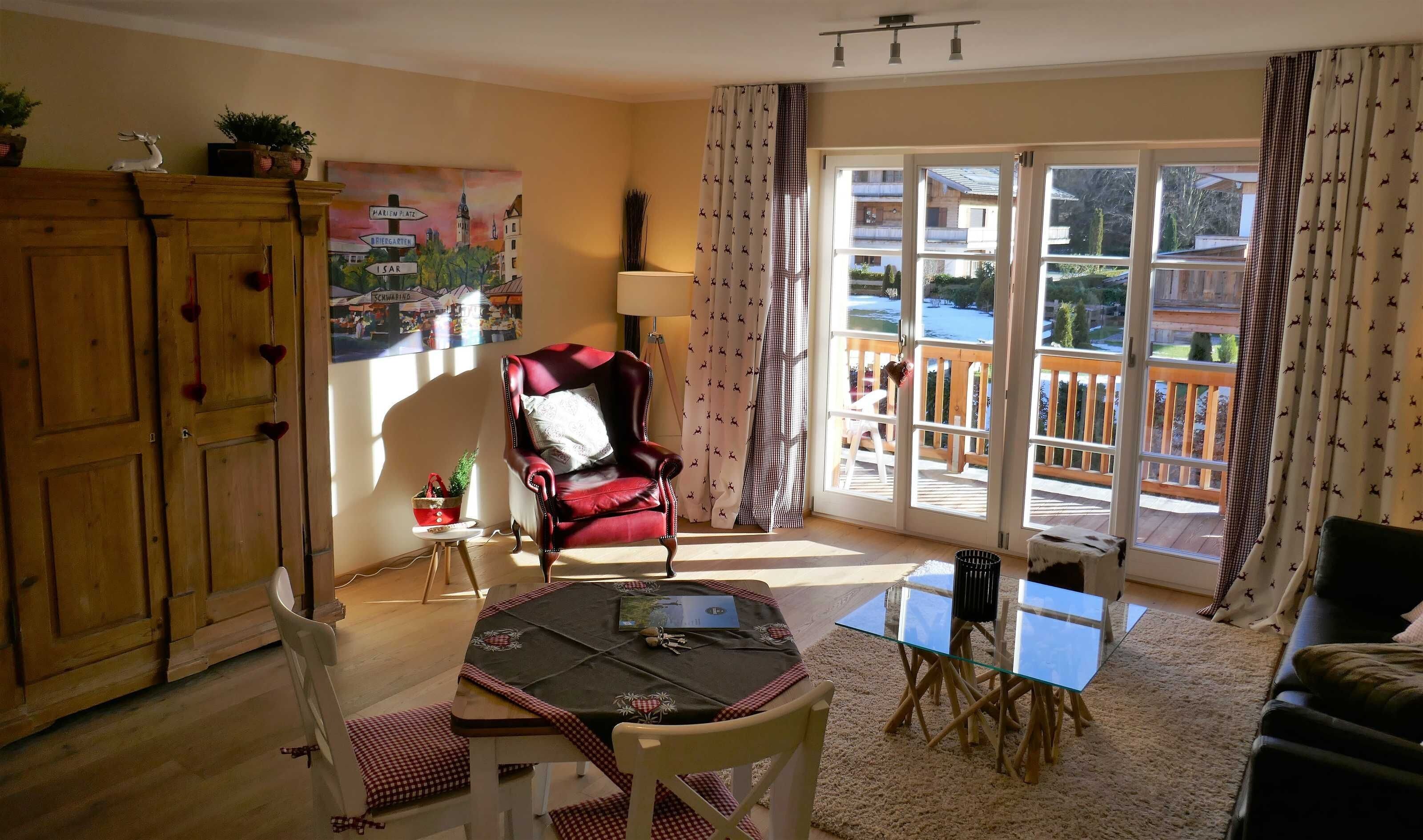 A room with a wooden cabinet, a red chair, a table with a glass top, and a view of a balcony through large windows.