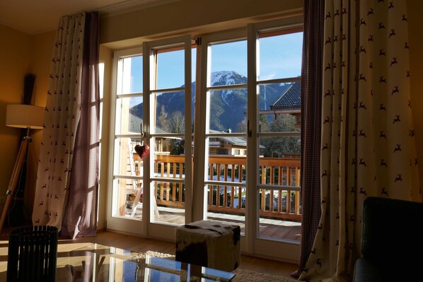 A room with large windows, a wooden deck, and a view of mountains.