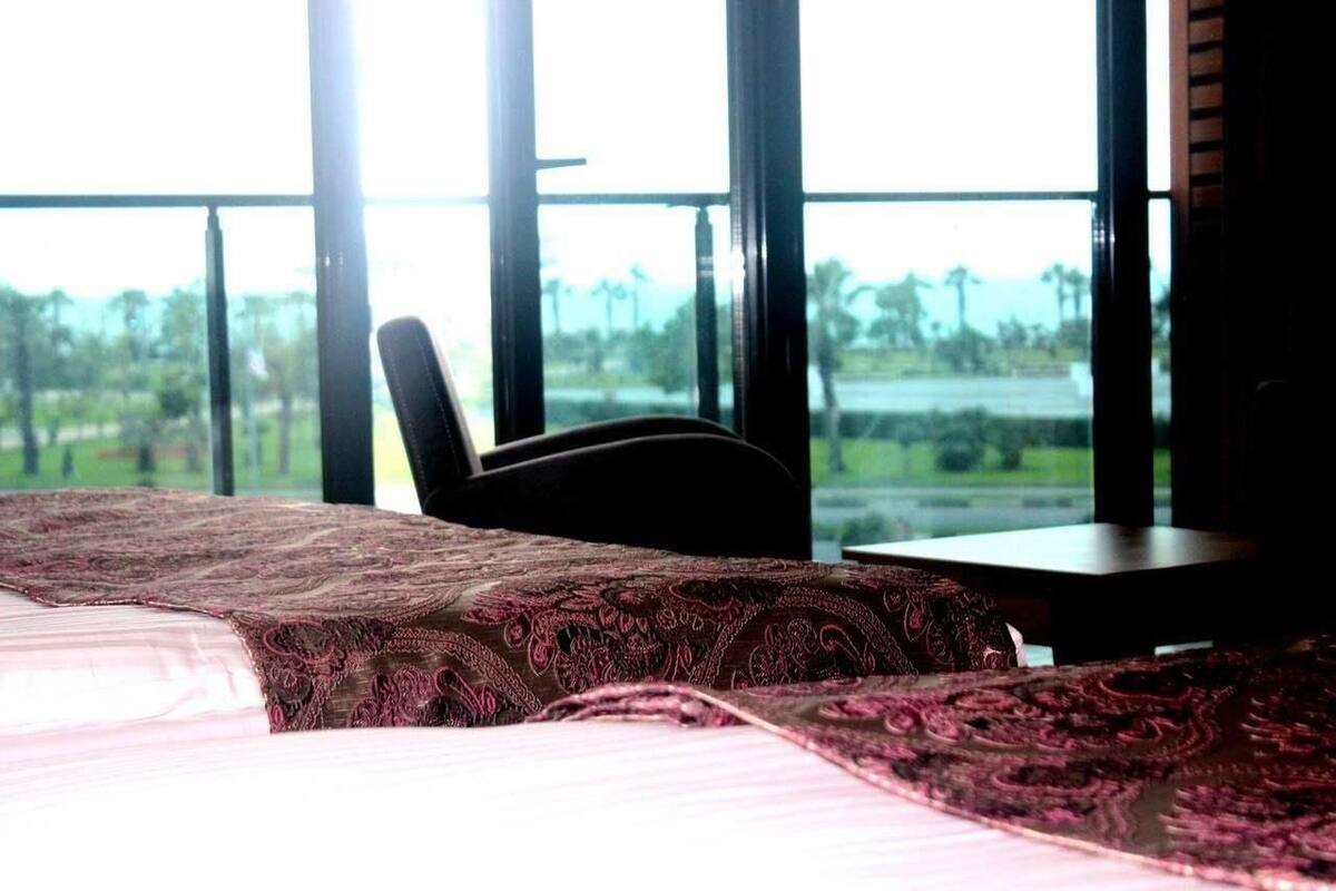 Habitación de hotel con una cama, una silla y una mesita. La habitación tiene ventanas amplias con vistas a zonas verdes.