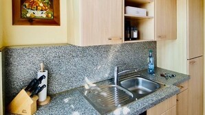 Une cuisine dotée de plans de travail en granit, d’un évier en acier inoxydable, de meubles en bois et d’une œuvre d’art encadrée accrochée au mur.