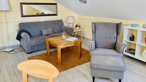 Un salon avec un canapé gris, une table basse en bois, un fauteuil gris et une petite table en bois.