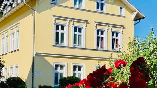 Un bâtiment à deux étages, avec une façade jaune et des ornements blancs.