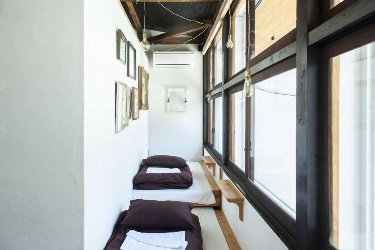 Un couloir étroit avec deux lits, des bancs en bois et de grandes fenêtres.