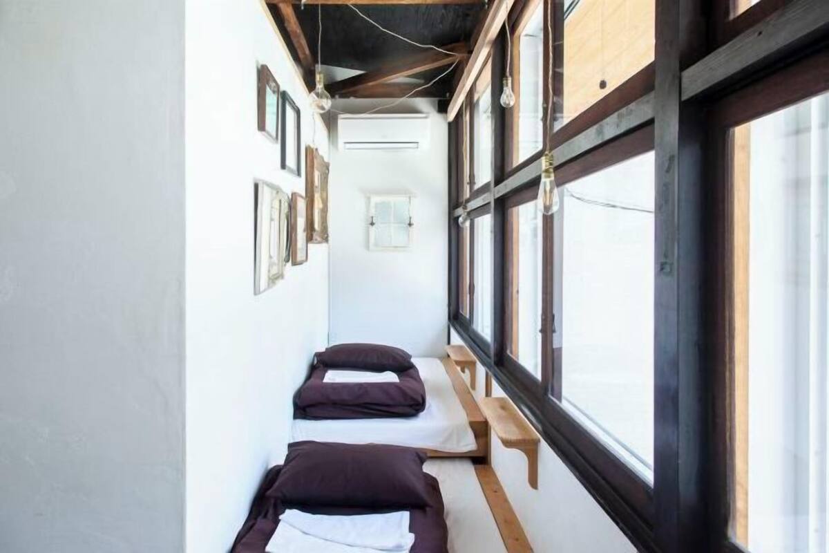 Un couloir étroit avec deux lits, des bancs en bois et de grandes fenêtres.
