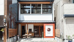 A two-story building with a wooden facade, a signboard, and a small outdoor seating area with tables and chairs. - Fukuoka Guesthouse HIVE - Hostel (Fukuoka)