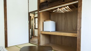 A room with tatami flooring, a low wooden table, a white refrigerator, and a wooden wardrobe with clothes hanging. - Fukuoka Guesthouse HIVE - Hostel (Fukuoka)