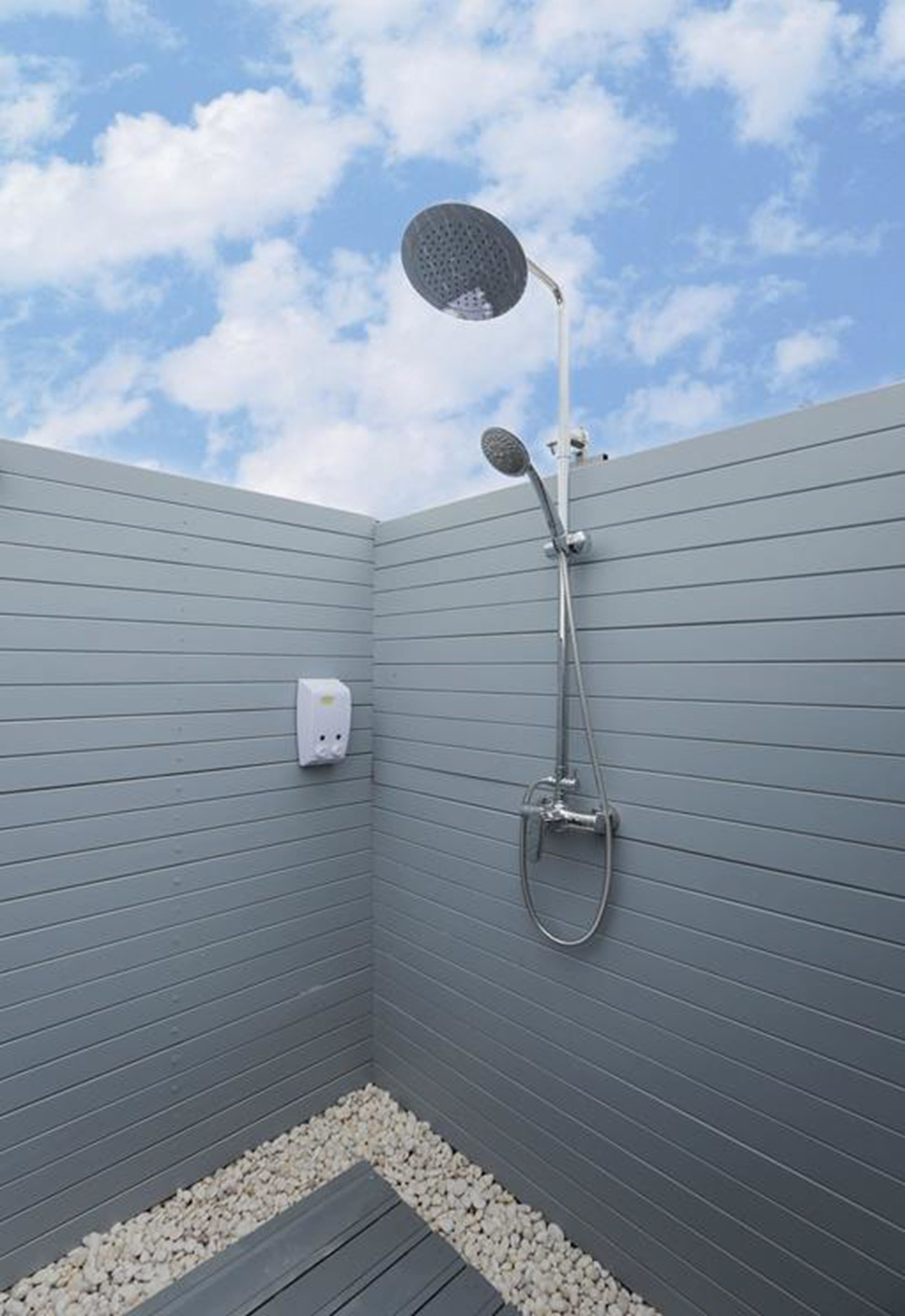 Una ducha moderna con cabezal de ducha de mano, panel de control en la pared y suelo cubierto de guijarros.
