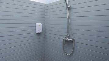 Una ducha moderna con cabezal de ducha de mano, panel de control en la pared y suelo cubierto de guijarros.