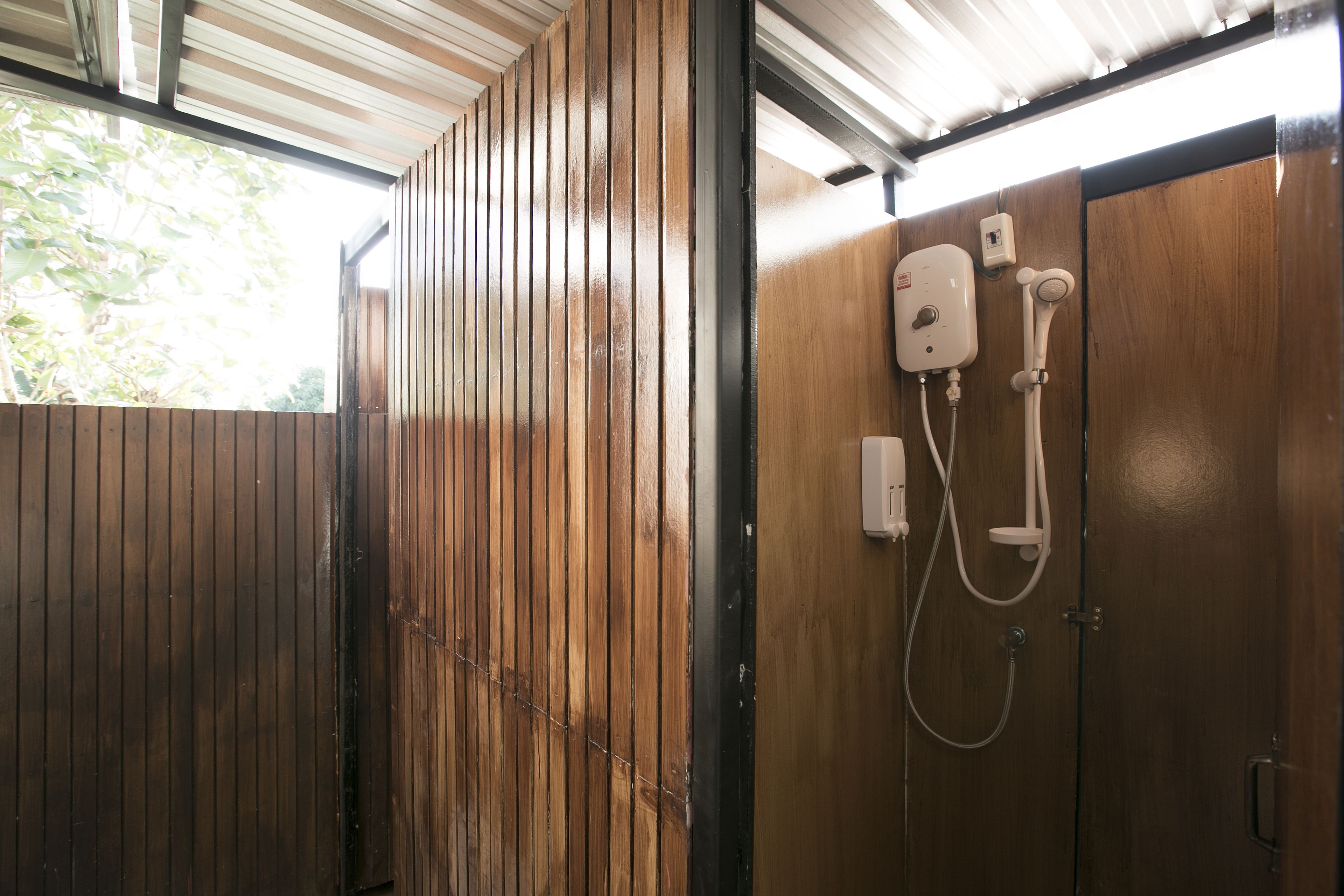A wooden partitioned bathroom with a shower area, including a showerhead and control panel.