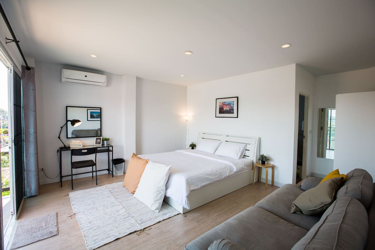 Ein modernes Schlafzimmer mit Bett, Schreibtisch, Stuhl, Sofa und einem kleinen Tisch mit Lampe.