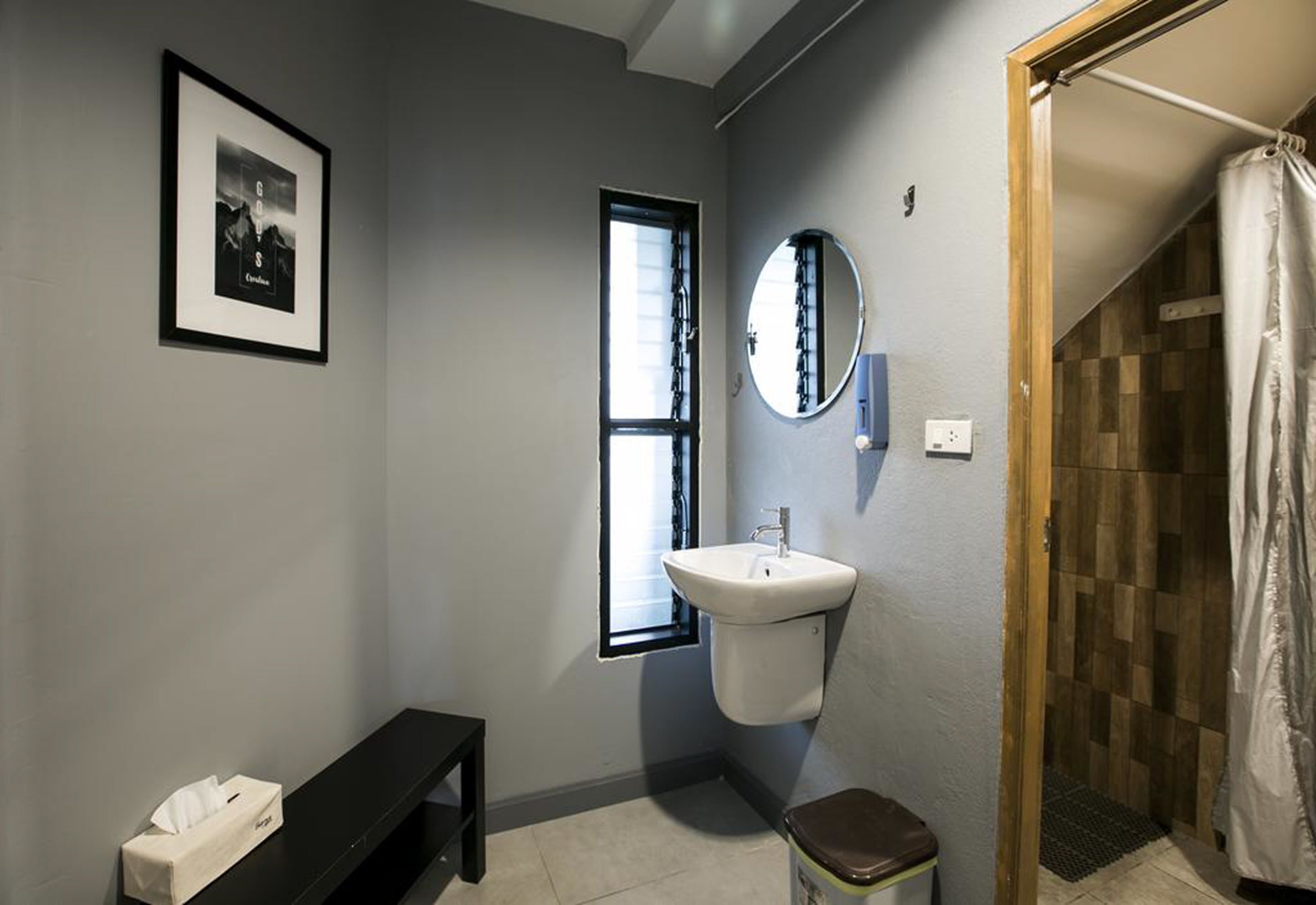 Un baño con un lavamanos blanco, un espejo, un cuadro enmarcado en la pared, un banco y una zona de ducha.