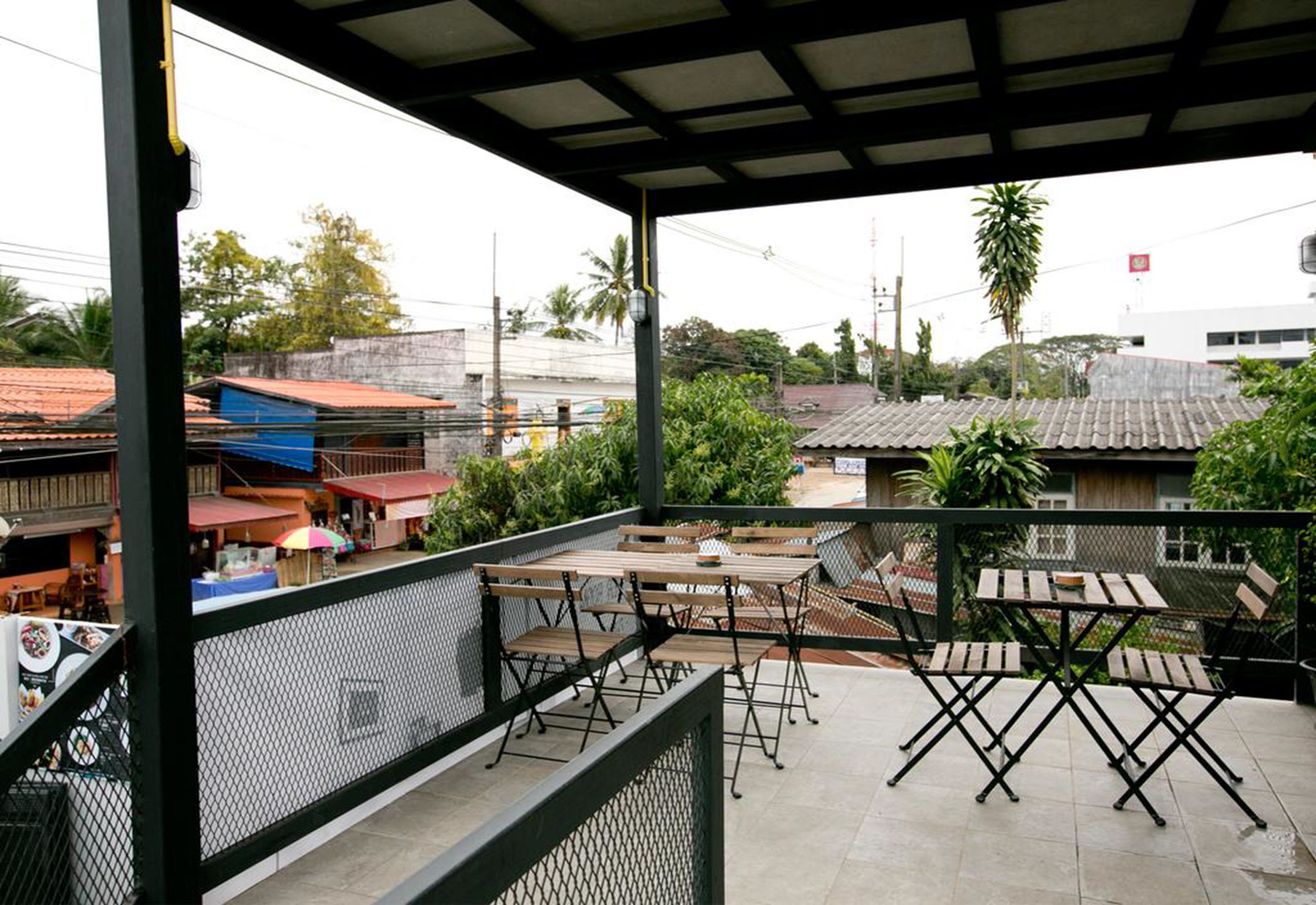 A covered outdoor seating area with tables and chairs, overlooking a residential neighborhood with houses and greenery.