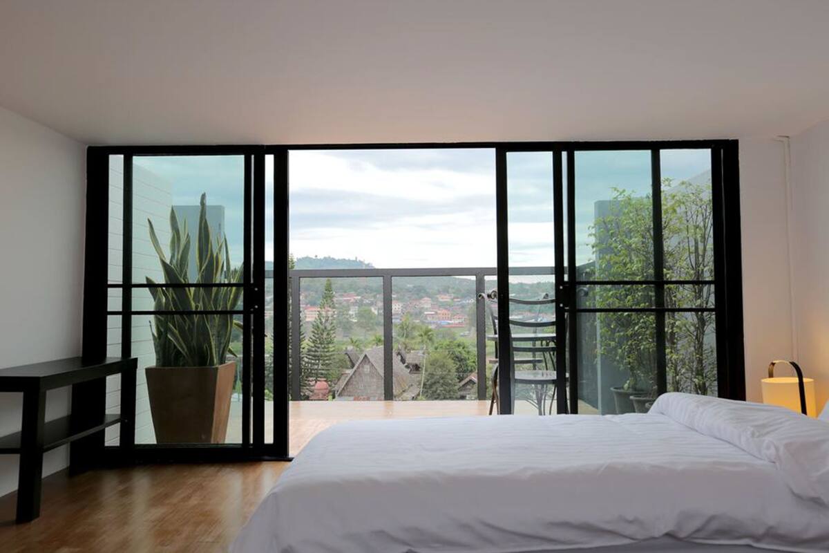 Ein Schlafzimmer mit großem Fenster, einem Bett, einer Bank und einem Blumentopf.