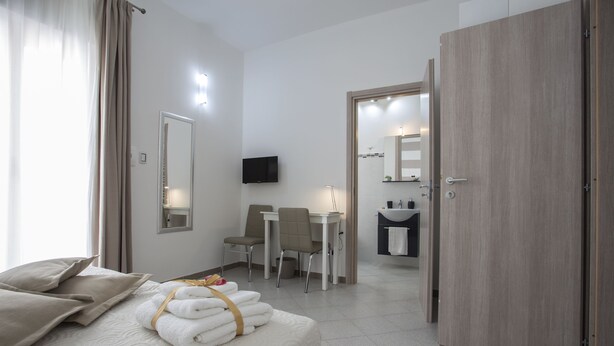 Habitación de hotel con cama, escritorio, silla, televisión y baño visible a través de una puerta abierta.