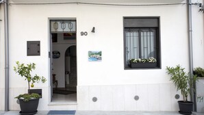 Entrada de un edificio con una puerta marcada '90', una ventana con una planta y dos macetas con plantas afuera.