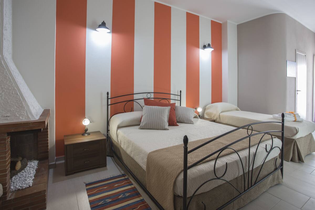 Une chambre à coucher avec un grand lit, une table de chevet, une commode, une cheminée et un mur à rayures.
