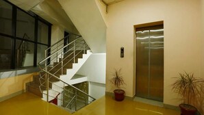 A modern interior with a staircase, elevator, and potted plants. - Hotel Green Lotus Dwarka (New Delhi)