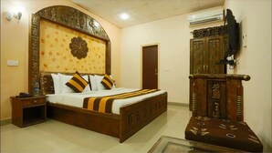 A bedroom with a large bed, a wooden headboard, a nightstand, a wardrobe, and a television mounted on the wall. - Hotel Green Lotus Dwarka (New Delhi)
