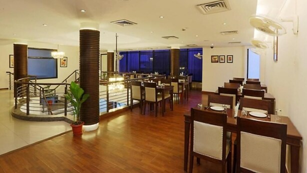 A spacious hotel lobby with a central staircase, multiple dining tables, and a large TV screen. - Hotel Green Lotus Dwarka (New Delhi)