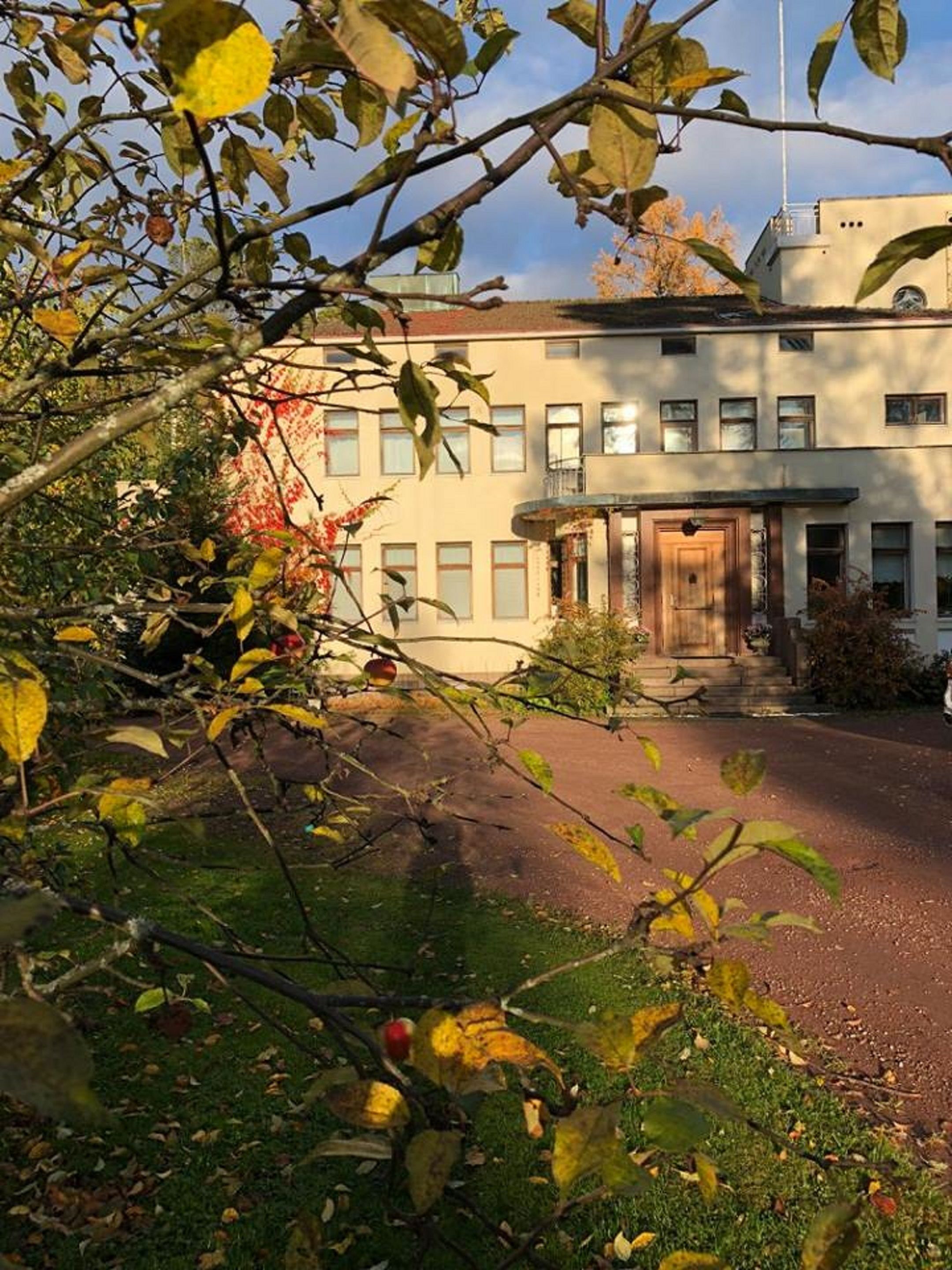 Un bâtiment doté d’une entrée centrale, entouré d’une zone pavée et d’arbres aux feuilles d’automne.