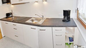 A compact kitchen with white cabinets, a stainless steel sink, a microwave, and a coffee maker. - Holiday home Bodden 47003 - Thatched cottage 47001 (Middelhagen)