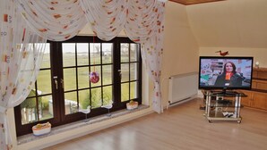 A living room with a large window, a television on a stand, and a view of the outdoors. - Holiday home Bodden 47003 - Thatched cottage 47001 (Middelhagen)