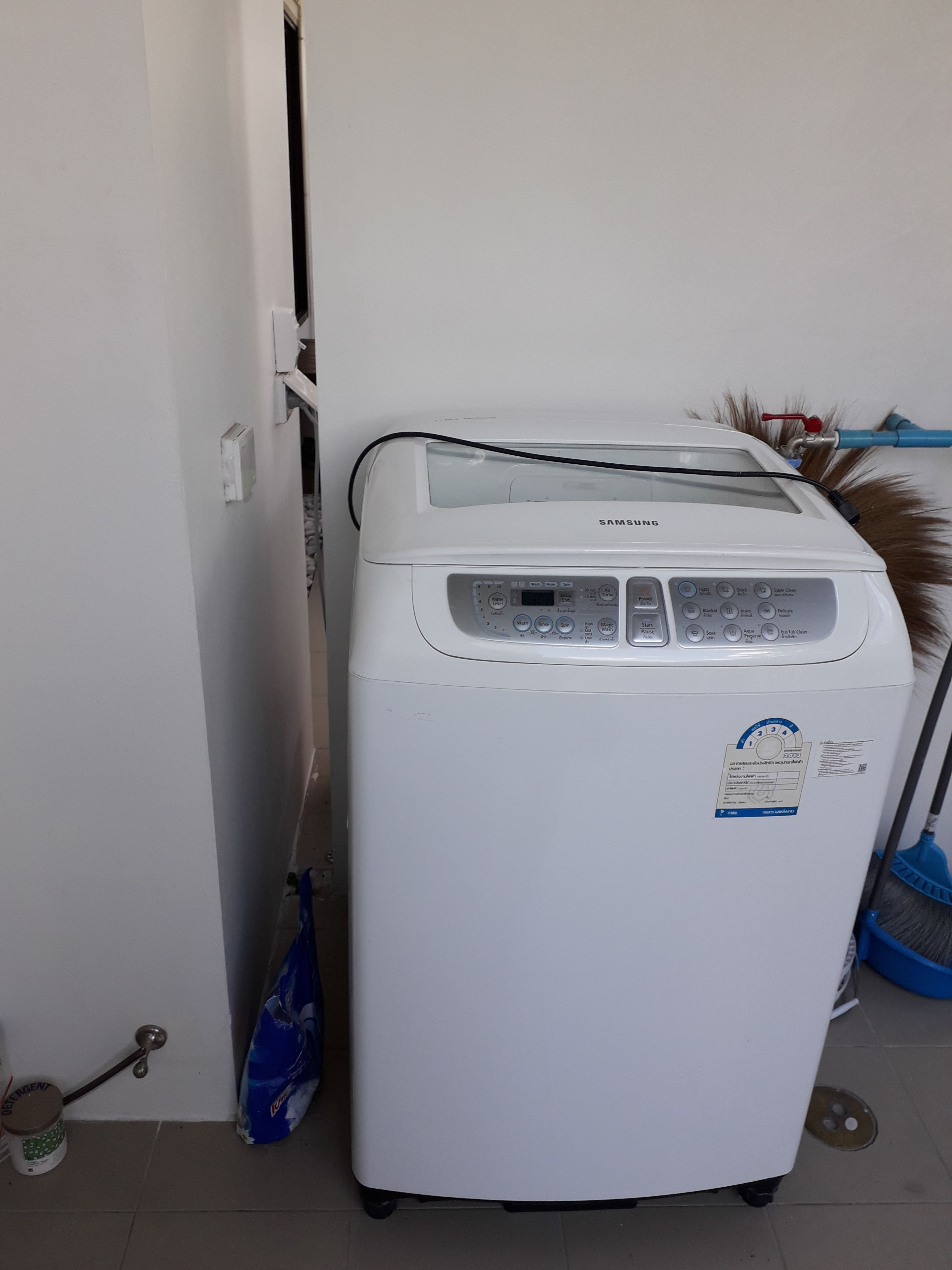 Una lavadora Samsung blanca en una habitación pequeña con suelo de baldosas.