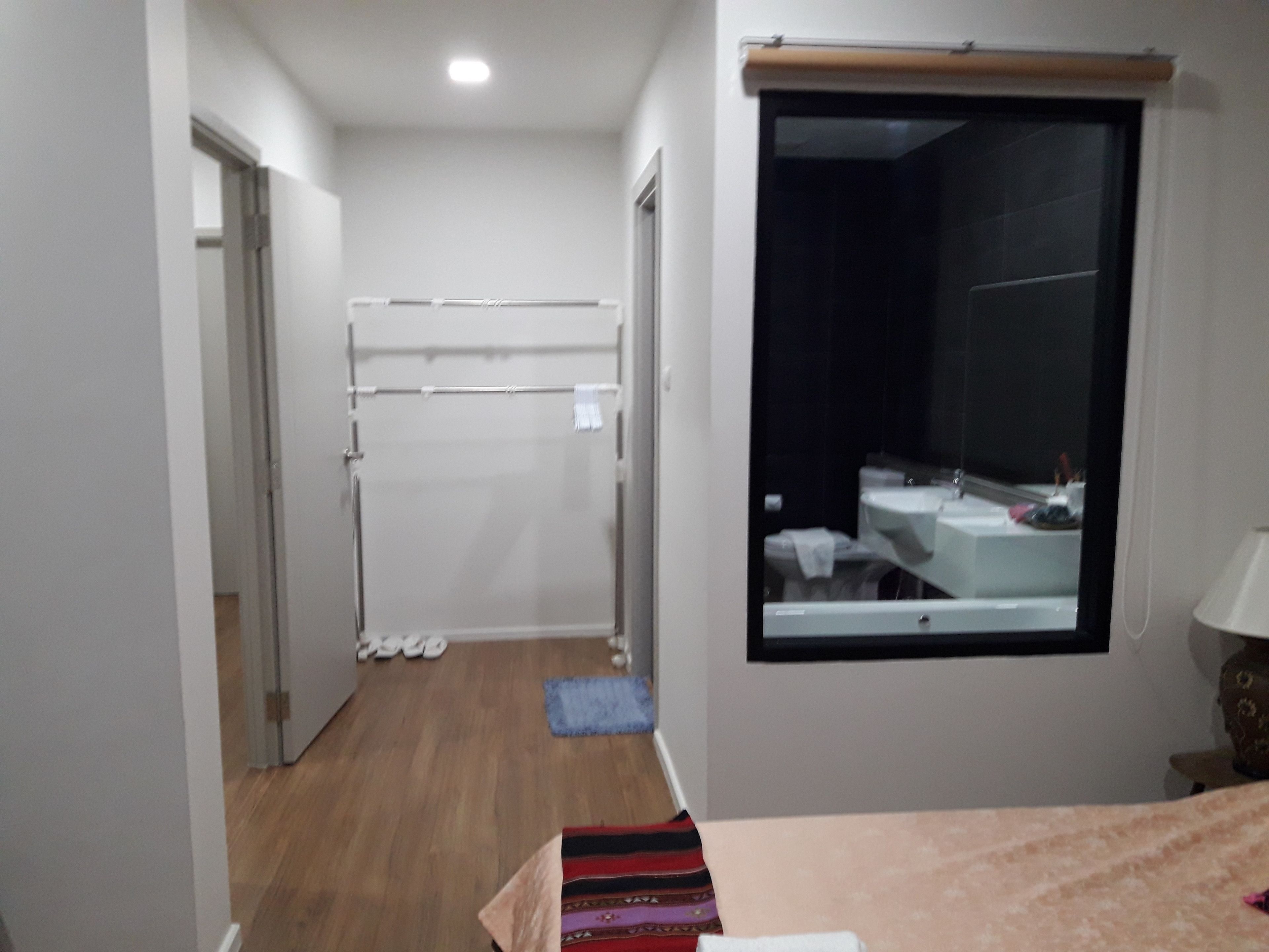Un pasillo estrecho que conduce a un baño con ventana, un perchero y una cama con colcha estampada.