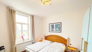 Un dormitorio con dos camas, una ventana con cortinas, un cuadro enmarcado en la pared y una mesita de noche con una lámpara.