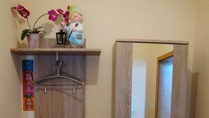Un armario de madera con espejo, una pequeña estantería con flores y una percha.