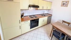 Una cocina compacta con estufa, fregadero, horno y una zona de comedor con mesa y sillas.