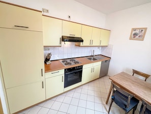 Cozinha compacta com fogão, pia, forno e área de refeições com mesa e cadeiras.